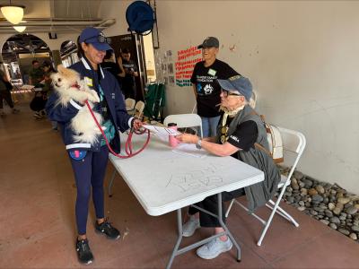 Person holding a small dog beside a table with people at the spay/neuter event