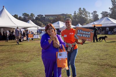 Smiling person holding small dog at the Best Friends Super Adoption in Los Angeles next to a person holding a sign that says, 'I found my BFF!'