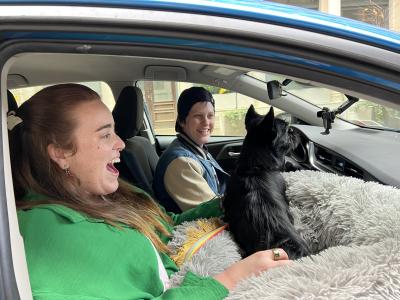 Two happy people in a vehicle with La Bamba the dog in the front seat
