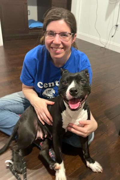 Smiling person hugging Nana, a black and white pit bull terrier