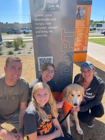 Caesar the dog with his new family outside in front of a Best Friends sign