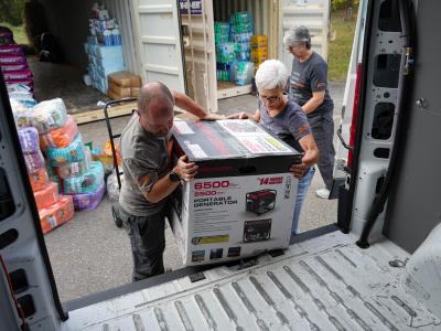Volunteer Toni Dorsey and another person lifting a portable generator in a box onto a truck