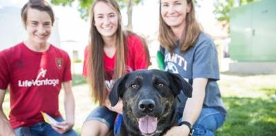 Two women and a man with a smiling dark dog