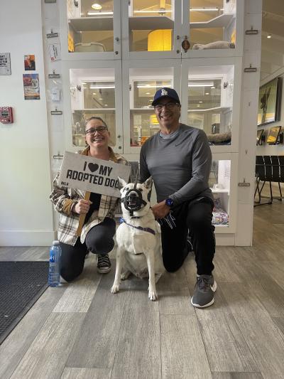 Magnus the dog with his new family, with one person holding a sign that says, 'I heart my adopted dog'