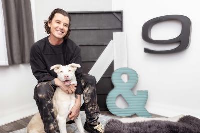 Gavin Rossdale hugging a white dog next to an & sign