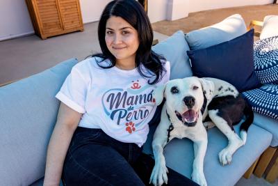 Person wearing a T-shirt that says Mama de Perro sitting on a couch next to a happy dog