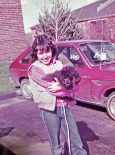 Mia Navedo-Williams in her early teens holding a dog standing in front of a car