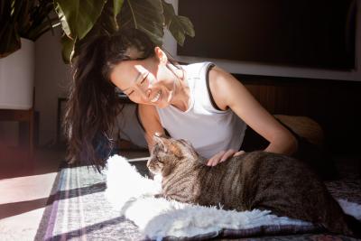 Person smiling and snuggling with a cat on the floor