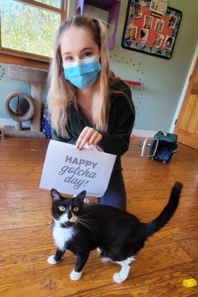 Miss Kitty with her masked adopter holding a sign that says, "Happy Gotcha Day!"