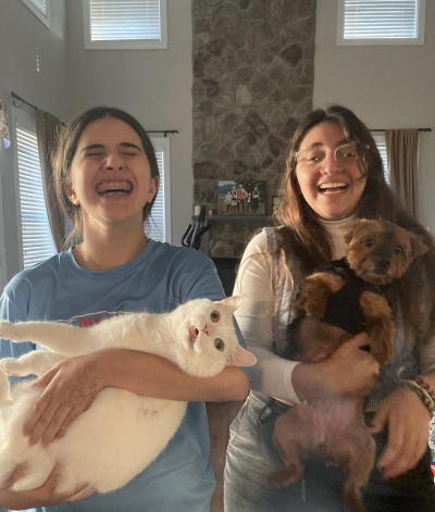 Laughing person holding Ollie the white, deaf cat next to another laughing person holding a small dog