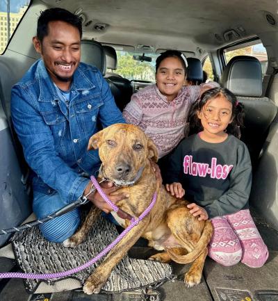 Smiling family in the back of a vehicle with a dog on a leash