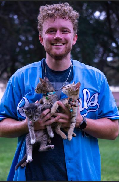 Smiling Mason Lange wearing a sports jersey and holding three tabby kittens