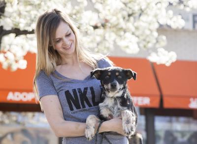 Woman holding smaller dog wearing an NKLA tee