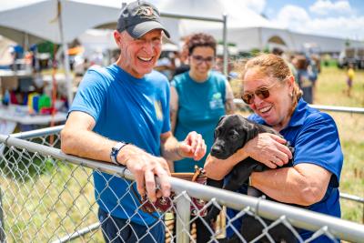 Three people in a chainlink pen with a small black puppy at the Best Friends Super Adoption in Northwest Arkansas