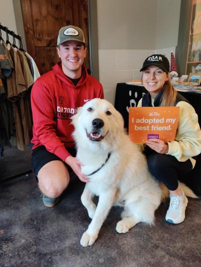 Teddy the great Pyrenees with his new adopters, who are holding a sign that says, "I adopted my best friend"