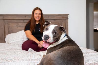 Smiling person with a dog sitting on a comfortable bed