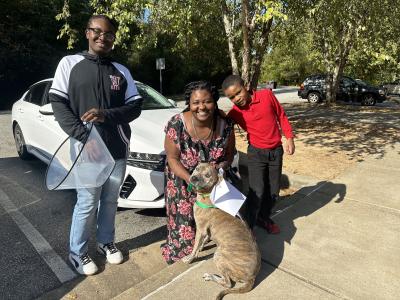 Family with brown brindle dog on a leash outside on front of a white car