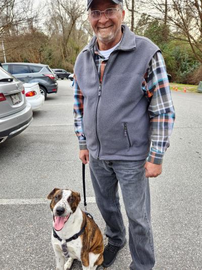 Smiling person walking a brindle and white dog outside on a leash