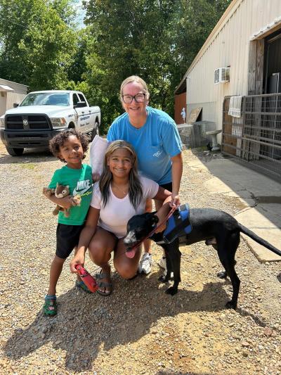 Three happy people outside with a black dog