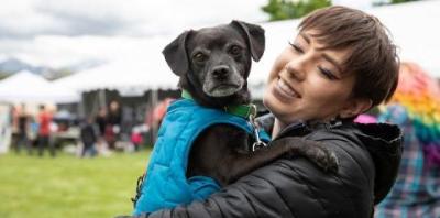 Woman with brown hair in black coat holding black dog in blue coat