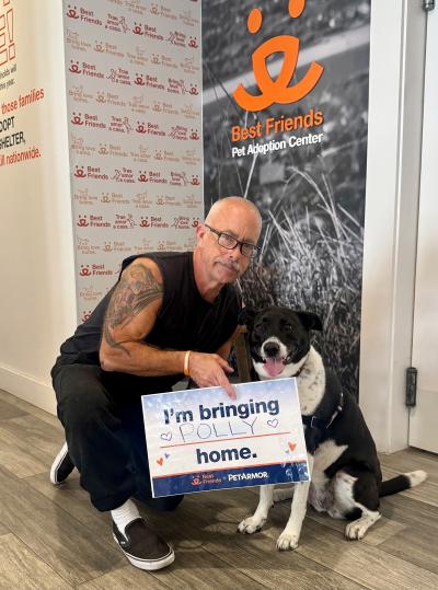 Polly beside her adopter who is holding a sign that says, 'I'm bringing Polly home.'