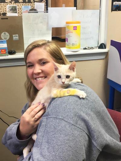 Smiling person holding a kitten with ringworm over her shoulder