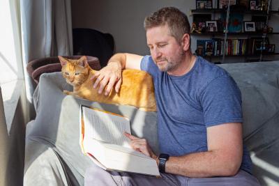 Person reading a book while petting an orange cat