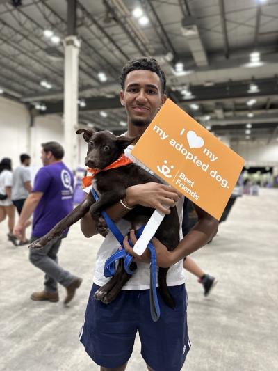 Person holding a puppy and a Best Friends sign that says, 'I heart my adopted dog'