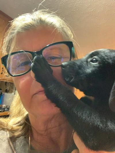 Lorri Simpson's face with a black puppy touching her face with a front paw