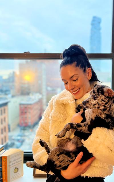 Liana next to a window and wearing a jacket holding Sonny the puppy