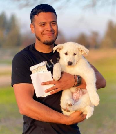 Smiling person holding a white puppy and paperwork