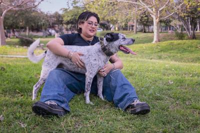 Person sitting on grass hugging a standing dog