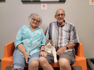 A couple sitting on an orange bench with Rufus the cat lying between them