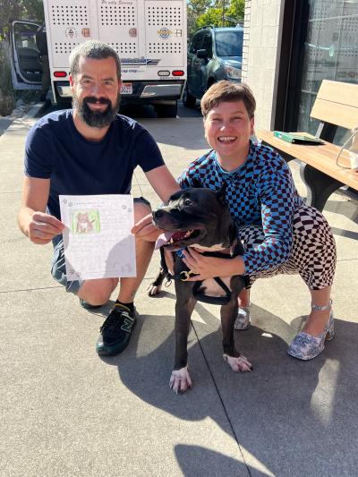 Tater the dog being adopted with his two people, one holding a piece of paper telling his story
