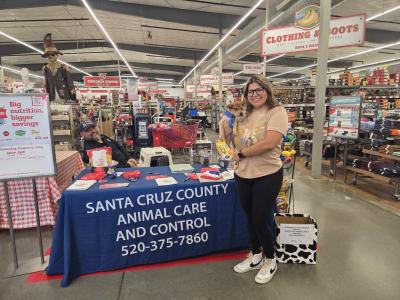 Person holding a puppy in front of a Santa Cruz County Animal Care and Control table at a store