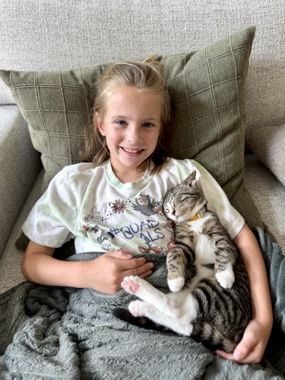 Child sitting on a chair with Sarah the kitten sleeping in her arm
