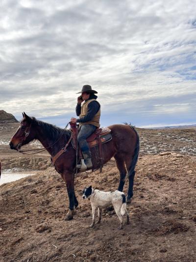 Skipper the dog on the ranch beside a person on a horse