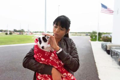 Person carrying a black and white puppy in a red blanket