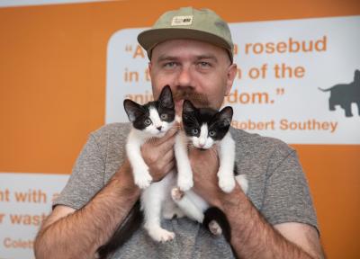 Foster volunteer Tyler Lisonbee holding two black and white kittens