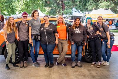 Volunteer Cheryl Baker in the center wearing orange surrounded by other people in front of an orange vehicle