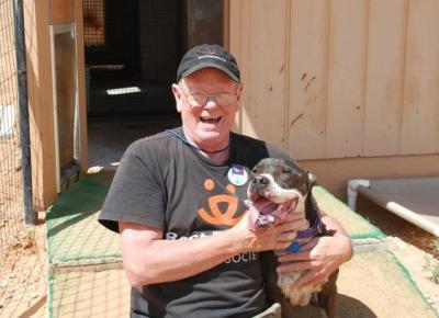 Volunteer Bill Splitter wearing a Best Friends T-shirt and smiling, holding a smiling dog