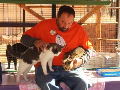 Russ Duszak wearing an orange T-shirt and volunteering at Cat World with two cats in his lap