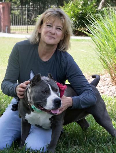 Volunteer Lisa Zarek sitting on the grass with a gray and white pit-bull-type dog with cropped ears