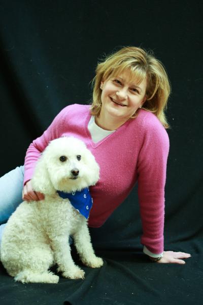 Volunteer Lisa Zarek posing with a small white poodle wearing a blue bandanna