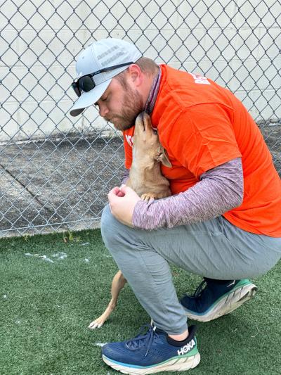 Best Friends in Houston takeover day volunteer receiving a kiss from a small brown dog