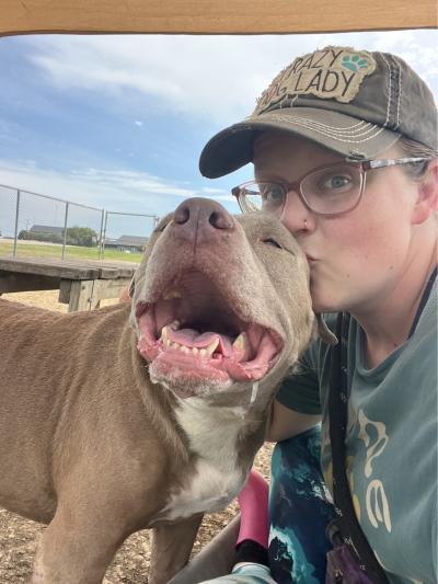 Person wearing a hat kissing the head of a happy dog