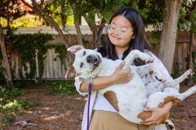 Shannon cradling Felix the dog in her arms while standing outside in a fenced yard