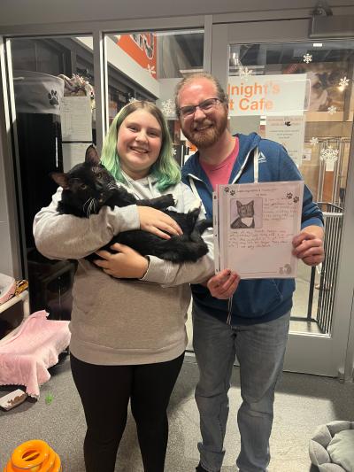 Hamburglar the cat with her two adopters, one who is holding a drawing and description of him