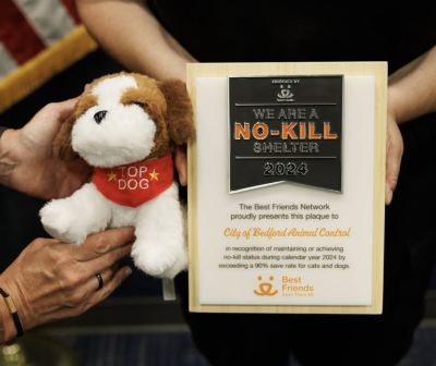 People's hands holding the Bedford Animal Shelter no-kill plaque and a stuffed dog