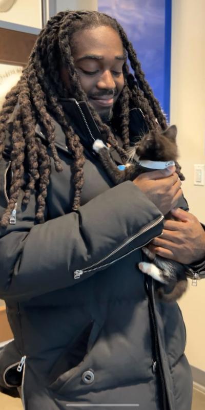 Smiling man wearing a heavy jacket holding a black and white kitten he'd just adopted
